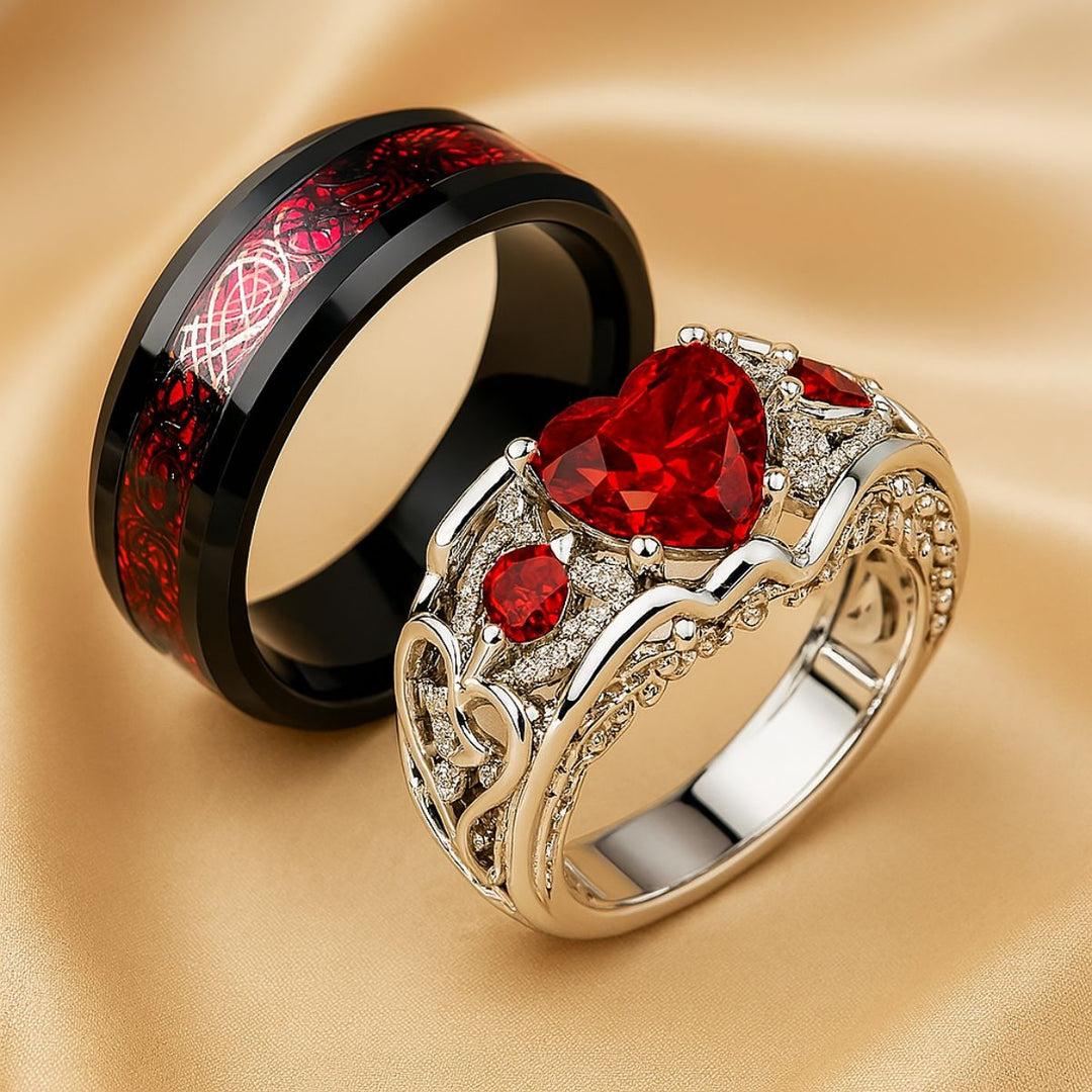 Cupid Arrow ring set from CouplesChoices.com, featuring a heart-shaped red gemstone in a filigree pavé band, paired with a black tungsten ring etched in crimson Celtic knotwork—crafted for eternal love.