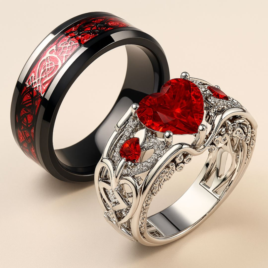 Cupid Arrow ring set from CouplesChoices.com, featuring a heart-shaped red gemstone in a filigree pavé band, paired with a black tungsten ring etched in crimson Celtic knotwork—crafted for eternal love.