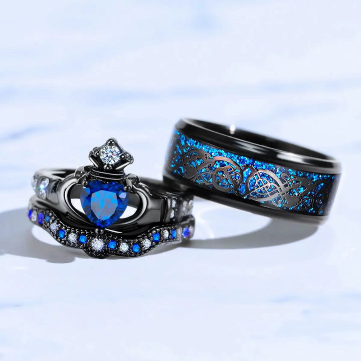 Elegant black titanium Unending Love ring set by CouplesChoices.com, featuring a sapphire heart, pavé-set stones, and a Celtic infinity pattern symbolizing eternal love.