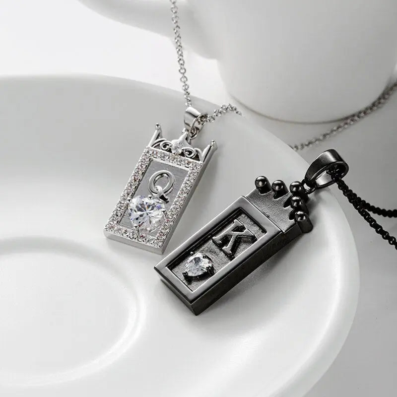 Matching King and Queen necklaces from CouplesChoices.com—black crown pendant with “K” for him and silver gem-framed pendant with “Q” for her. A bold, regal expression of love, loyalty, and royal couple energy.