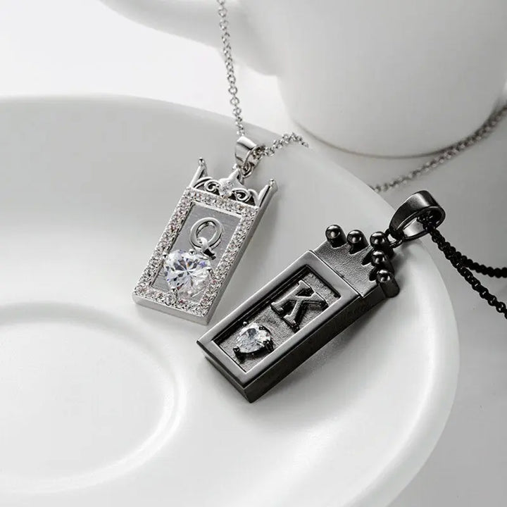 Matching King and Queen necklaces from CouplesChoices.com—black crown pendant with “K” for him and silver gem-framed pendant with “Q” for her. A bold, regal expression of love, loyalty, and royal couple energy.