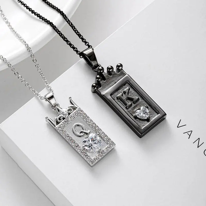 Matching King and Queen necklaces from CouplesChoices.com—black crown pendant with “K” for him and silver gem-framed pendant with “Q” for her. A bold, regal expression of love, loyalty, and royal couple energy.