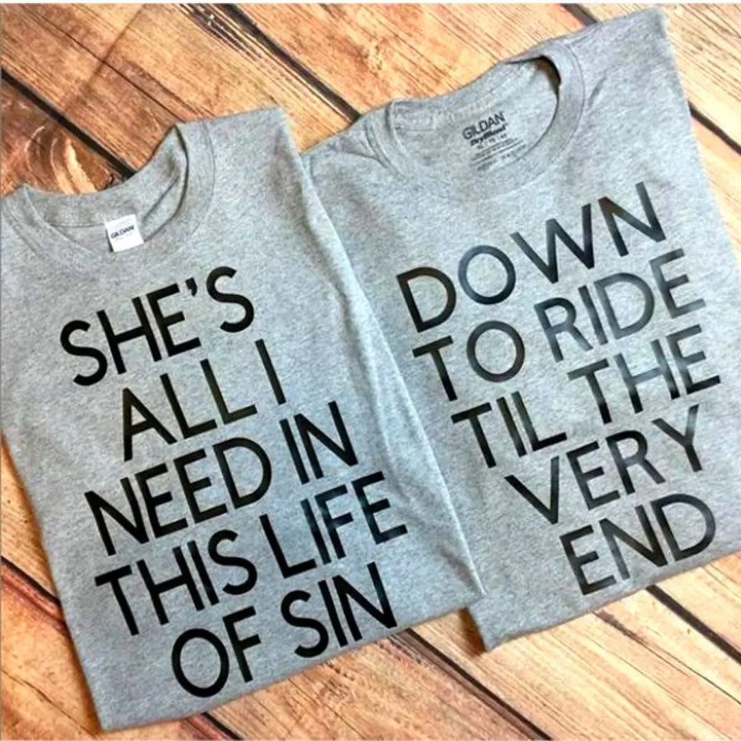 Couples’ matching grey tees with bold black text—his reads ‘She’s all I need in this life of sin,’ hers says ‘Down to ride til the very end.’ A fearless, ride-or-die statement set from CouplesChoices.com.
