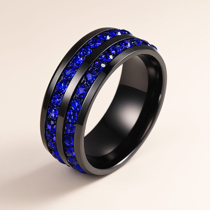 Blue Inspiration Ring Set by CouplesChoices.com featuring a radiant-cut sapphire-blue center stone on a sleek black band, flanked by pavé-set royal blue stones, paired with a matching eternity-style men’s band—crafted for bold connection.