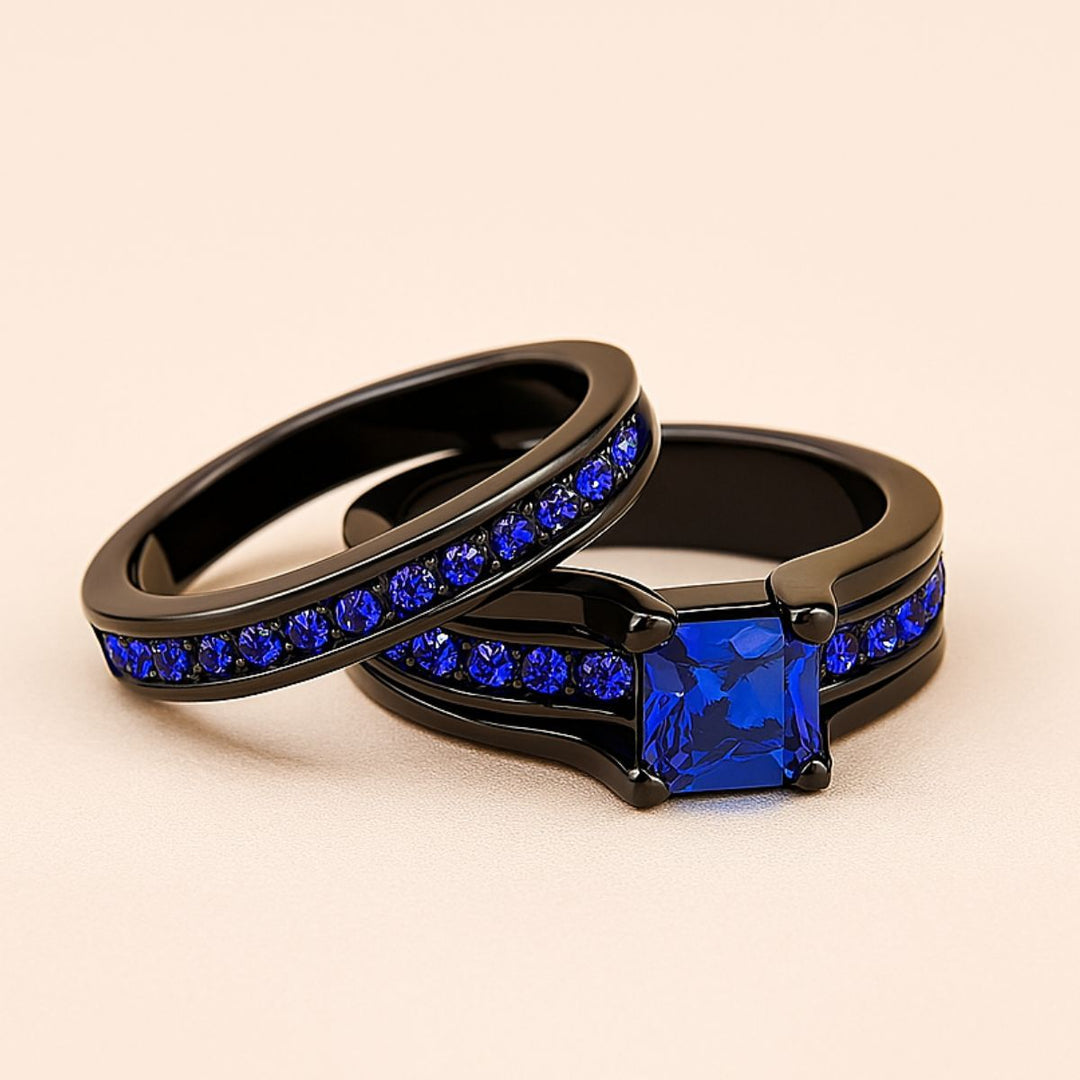 Blue Inspiration Ring Set by CouplesChoices.com featuring a radiant-cut sapphire-blue center stone on a sleek black band, flanked by pavé-set royal blue stones, paired with a matching eternity-style men’s band—crafted for bold connection.