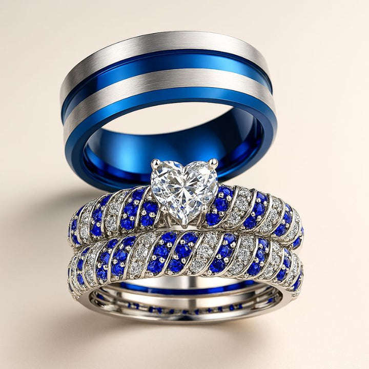 Blue Ocean wedding ring set from CouplesChoices.com, featuring a heart-shaped center stone flanked by pavé-set blue and white crystals in a twisted silver band, paired with a brushed silver and cobalt blue men's band.