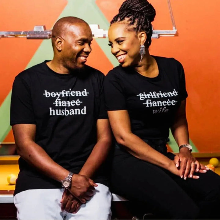  Couples' black matching tees—his shows 'boyfriend' and 'fiancé' crossed out with 'husband' below, hers reads 'girlfriend' and 'fiancée' crossed out with 'wife' below. A love story told in text, from CouplesChoices.com.