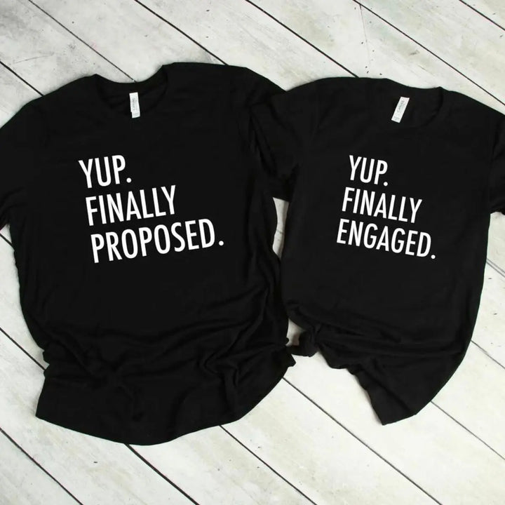 Couples' matching black tees—his says 'Yup. Finally Proposed.' and hers reads 'Yup. Finally Engaged.' Bold white text for couples ready to celebrate the moment. Exclusively from CouplesChoices.com.