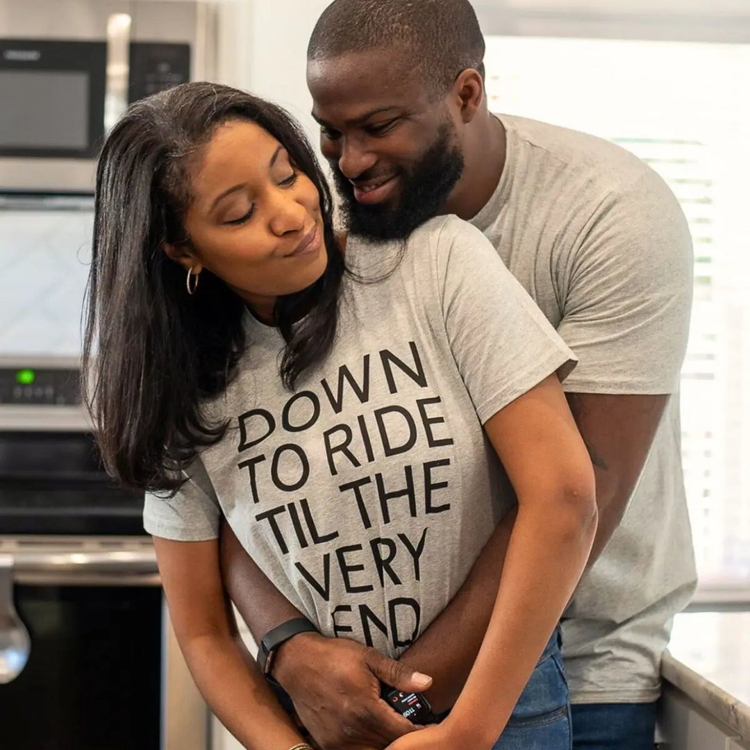 Couples’ matching grey tees with bold black text—his reads ‘She’s all I need in this life of sin,’ hers says ‘Down to ride til the very end.’ A fearless, ride-or-die statement set from CouplesChoices.com.