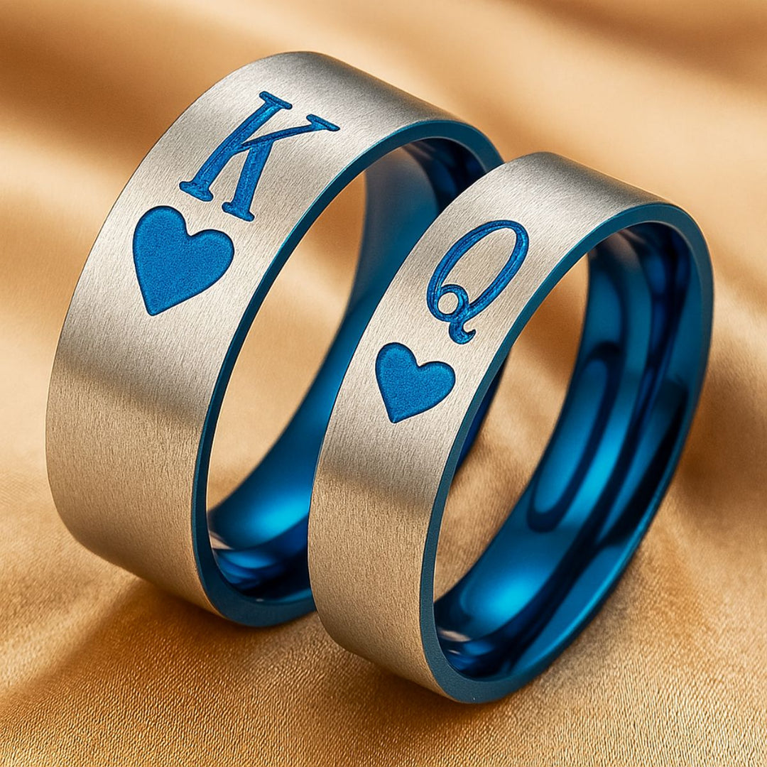Elegant Royal Harbour Rings from CouplesChoices.com, featuring brushed silver bands with bold blue heart inlays and 'K' & 'Q' engravings—symbolizing King and Queen. A striking emblem of love, loyalty, and regal partnership.