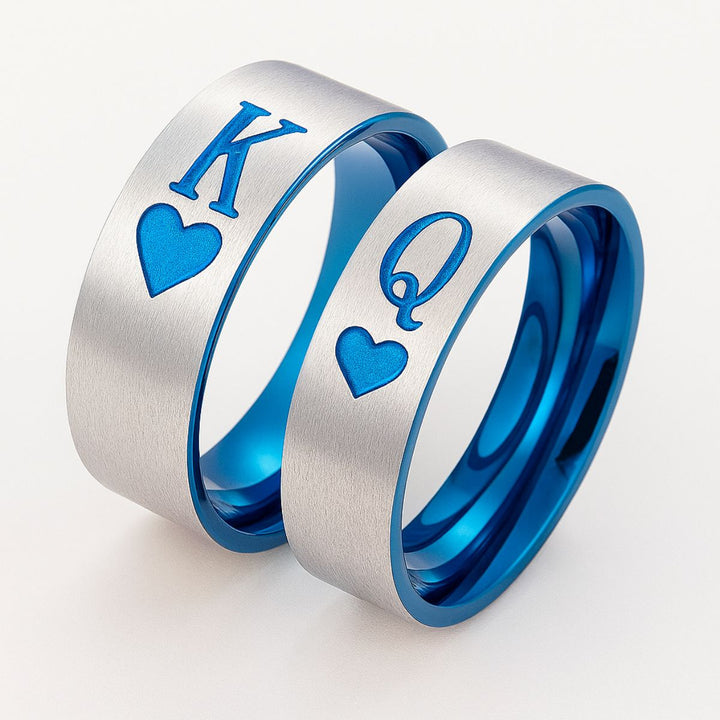Elegant Royal Harbour Rings from CouplesChoices.com, featuring brushed silver bands with bold blue heart inlays and 'K' & 'Q' engravings—symbolizing King and Queen. A striking emblem of love, loyalty, and regal partnership.