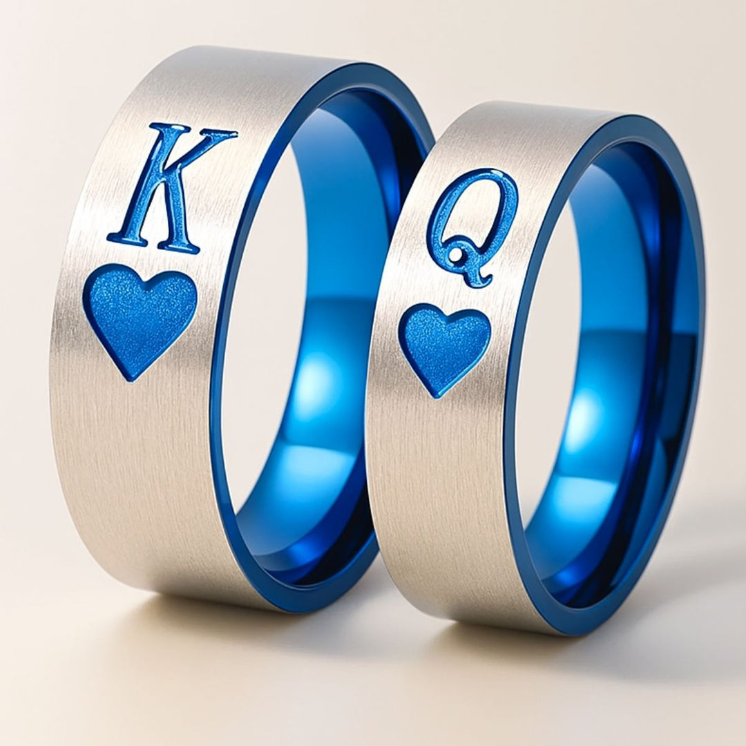 Elegant Royal Harbour Rings from CouplesChoices.com, featuring brushed silver bands with bold blue heart inlays and 'K' & 'Q' engravings—symbolizing King and Queen. A striking emblem of love, loyalty, and regal partnership.