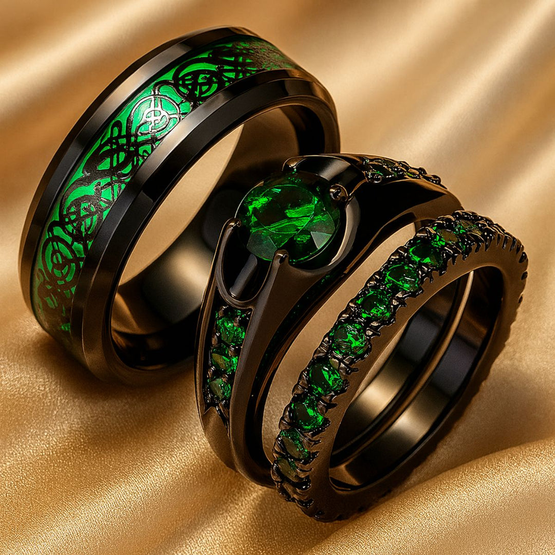 Emerald Love ring set by CouplesChoices.com, featuring a radiant green gemstone trio on black-plated bands and a matching men’s ring with shimmering emerald Celtic knotwork—bold, modern, eternal.