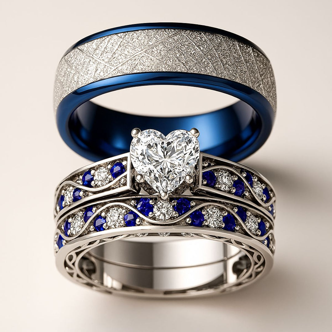 Fiesta ring set by CouplesChoices.com, featuring a radiant heart-cut diamond centerpiece with blue and white stones in a flowing wave design, paired with a silver and sapphire-toned textured band.