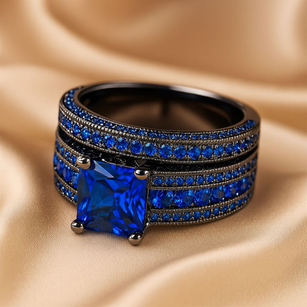 Love Dance ring set by CouplesChoices.com, featuring a bold black titanium band with electric blue inlay and a radiant princess-cut sapphire atop pavé-set blue stones—designed to move hearts.