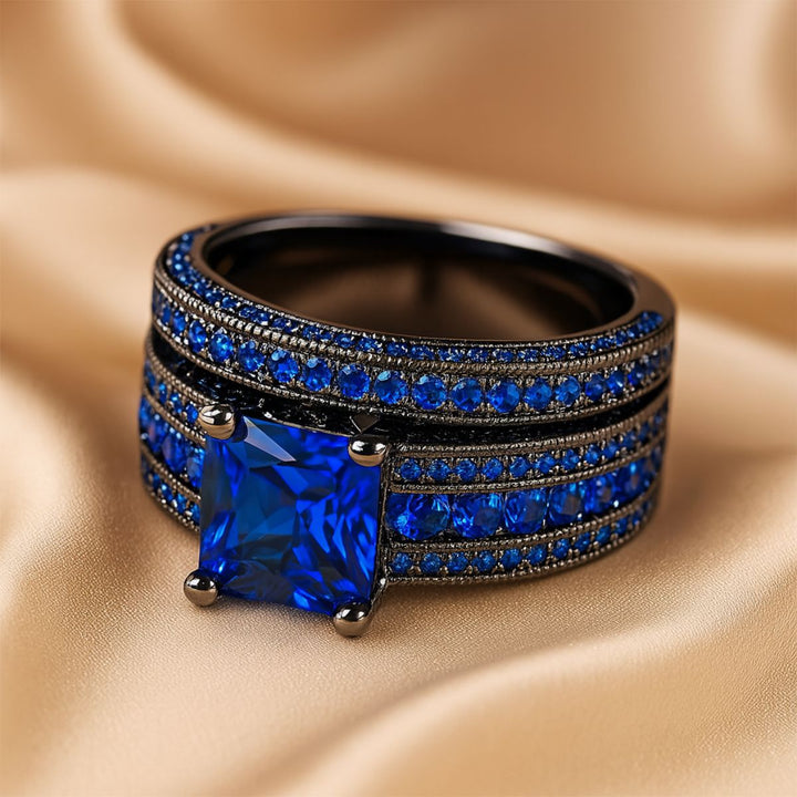 Love Dance ring set by CouplesChoices.com, featuring a bold black titanium band with electric blue inlay and a radiant princess-cut sapphire atop pavé-set blue stones—designed to move hearts.