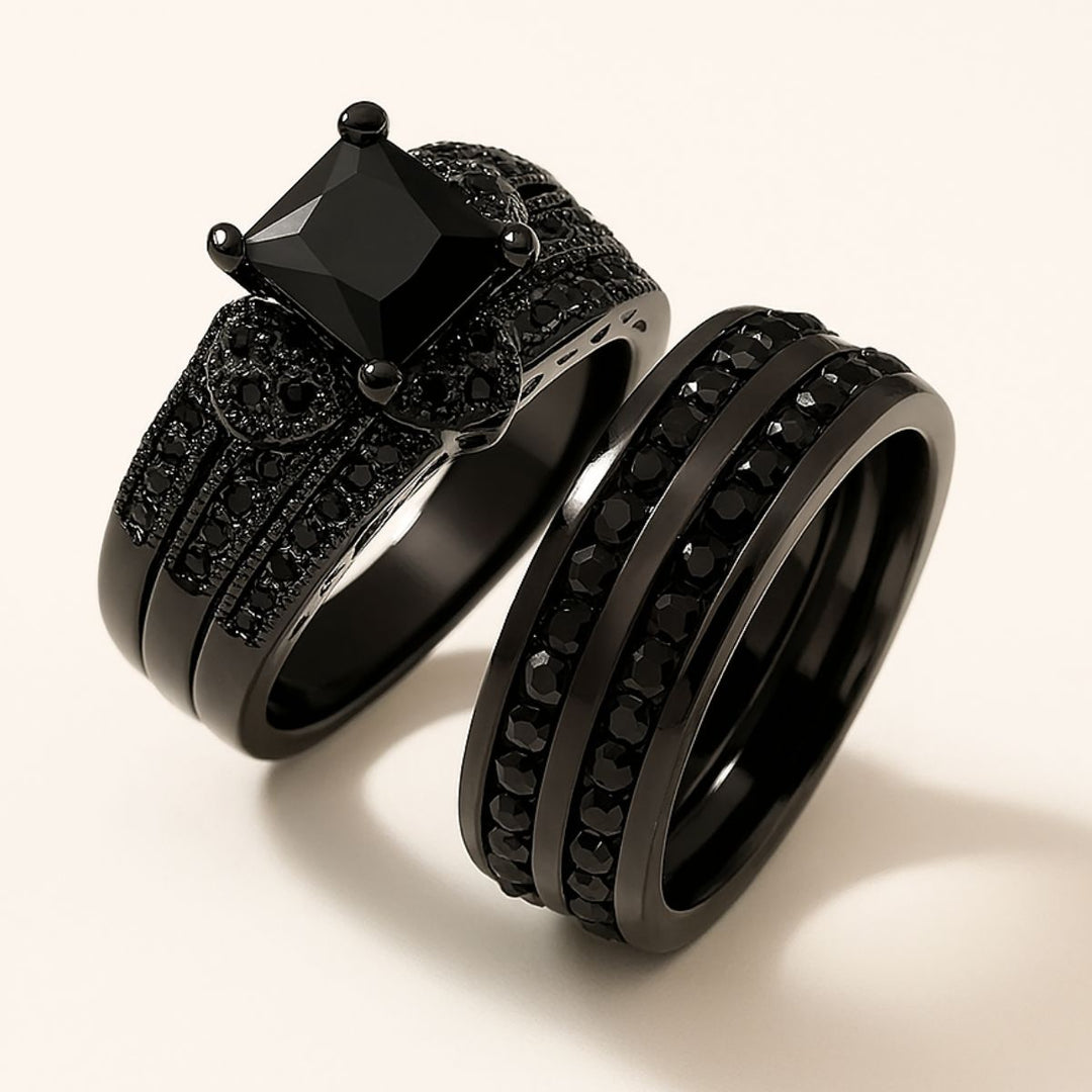 Love Glory Rings from CouplesChoices.com, featuring a bold princess-cut black diamond ring surrounded by pavé-set black stones and heart-shaped accents, paired with a matching dual-row black diamond band — a striking symbol of everlasting love.