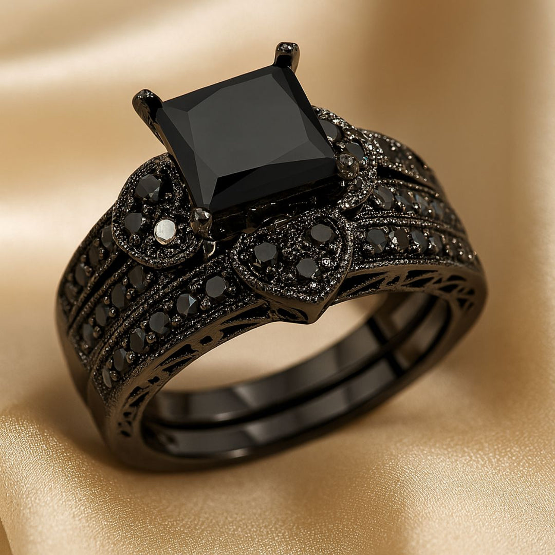 Love Glory Rings from CouplesChoices.com, featuring a bold princess-cut black diamond ring surrounded by pavé-set black stones and heart-shaped accents, paired with a matching dual-row black diamond band — a striking symbol of everlasting love.