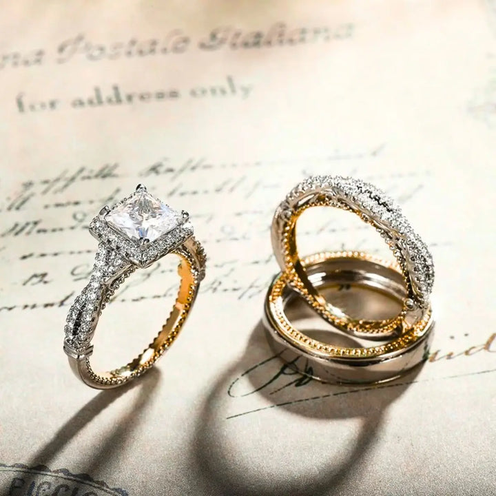 Lumina ring set by CouplesChoices.com, showcasing a princess-cut center stone on a pavé infinity band in radiant gold, paired with a matching gold men’s band for a timeless, luminous union.