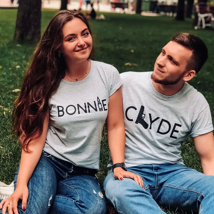 Matching Bonnie & Clyde couple shirts in soft heather grey, featuring bold black text with a gun and bullet design. Perfect for ride-or-die couples who love bold style and iconic vibes. Exclusively from CouplesChoices.com.