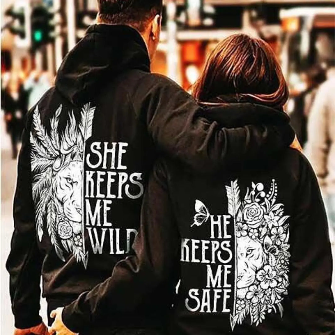 Matching black couple hoodies from CouplesChoices.com featuring powerful lion-themed designs — “She Keeps Me Wild” with feathers and “He Keeps Me Safe” with floral elements. A bold, symbolic set for couples who balance passion with protection.