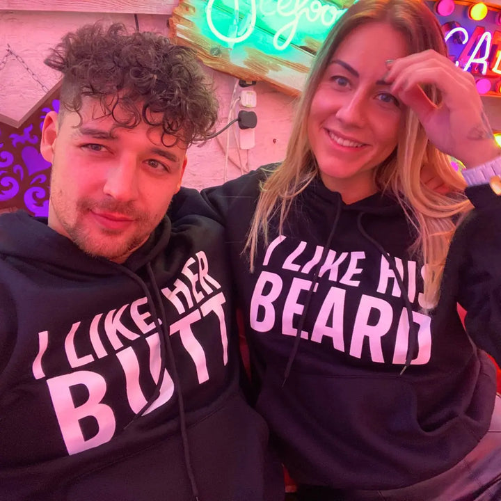 Matching black couple hoodies with bold white text — “I LIKE HER BUTT” on his and “I LIKE HIS BEARD” on hers — from CouplesChoices.com. Fun, flirty, and perfect for couples who love playful, stylish matching outfits.