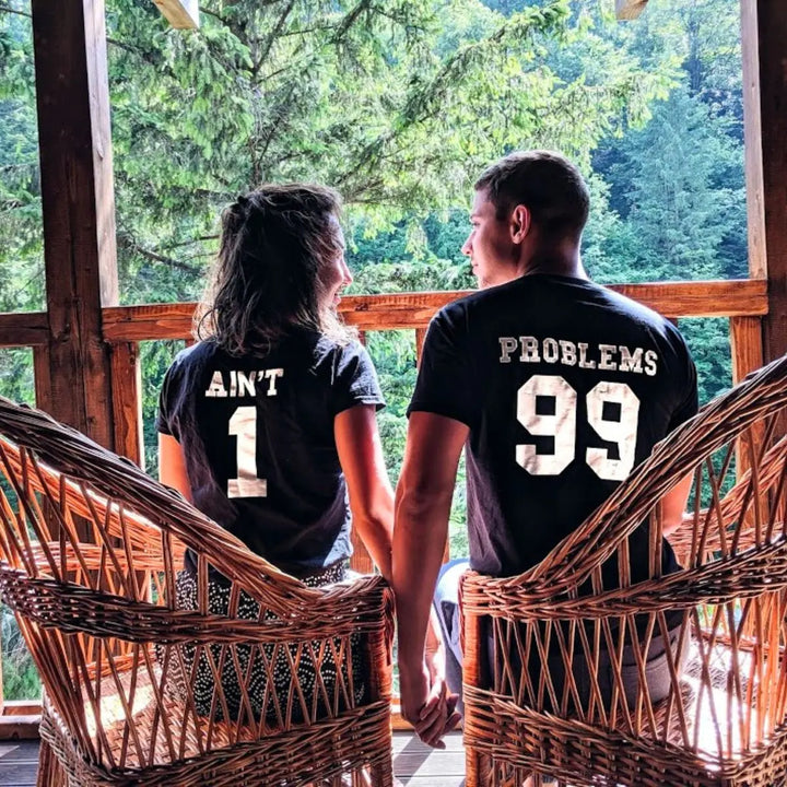 Matching black couple shirts—his reads '99 Problems' and hers answers 'Ain’t 1' in varsity-style white print. A playful nod to love and loyalty, exclusively from CouplesChoices.com.