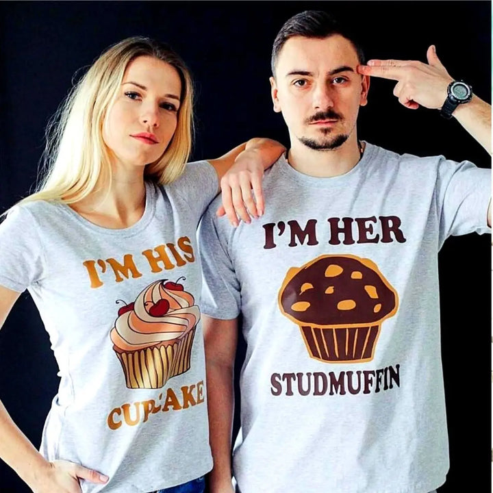 Adorably cheeky couple shirts in heather grey—hers says 'I’m His Cupcake' with a frosted treat, his reads 'I’m Her Studmuffin' with a chocolate muffin. A sweet and playful pair from CouplesChoices.com.