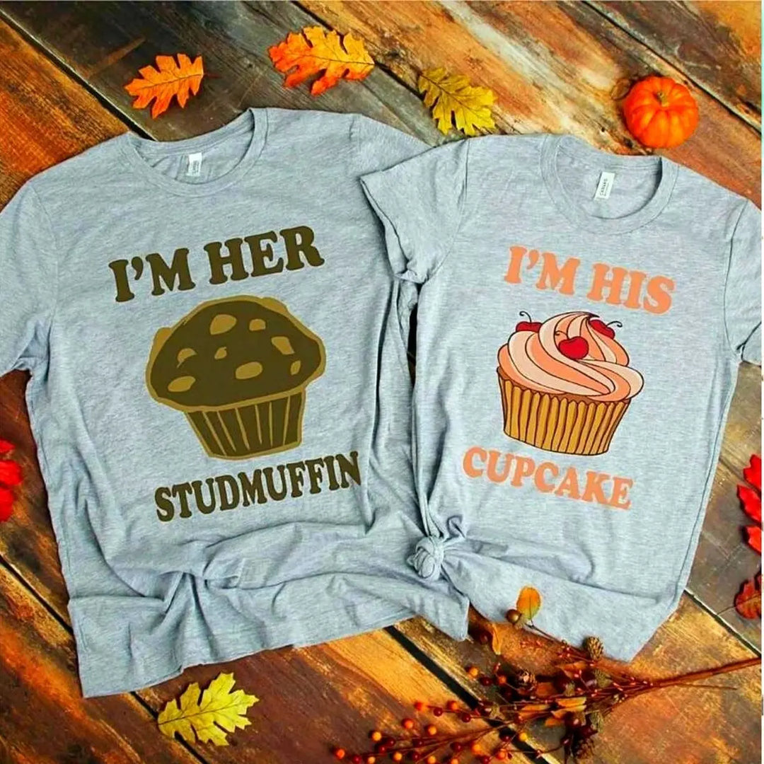 Adorably cheeky couple shirts in heather grey—hers says 'I’m His Cupcake' with a frosted treat, his reads 'I’m Her Studmuffin' with a chocolate muffin. A sweet and playful pair from CouplesChoices.com.