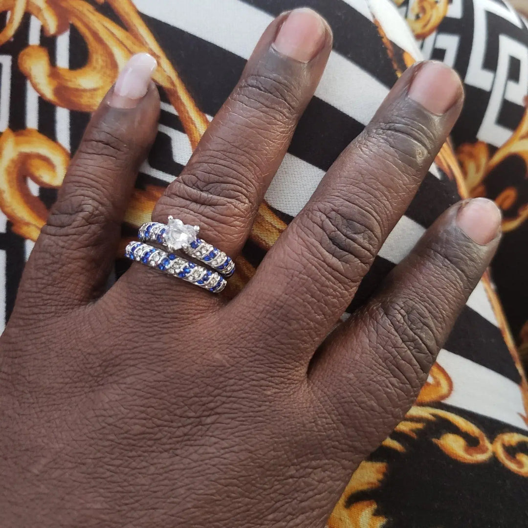 Blue Ocean wedding ring set from CouplesChoices.com, featuring a heart-shaped center stone flanked by pavé-set blue and white crystals in a twisted silver band, paired with a brushed silver and cobalt blue men's band.