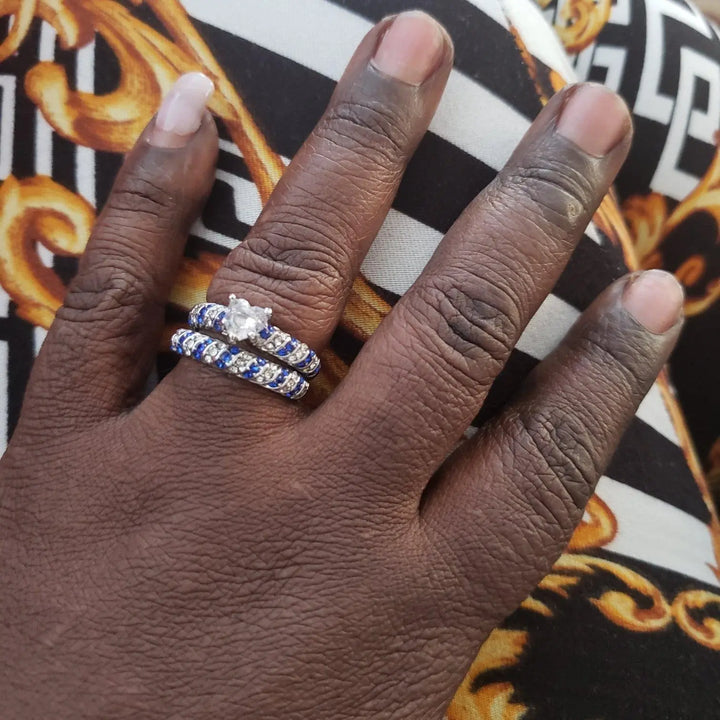 Blue Ocean wedding ring set from CouplesChoices.com, featuring a heart-shaped center stone flanked by pavé-set blue and white crystals in a twisted silver band, paired with a brushed silver and cobalt blue men's band.