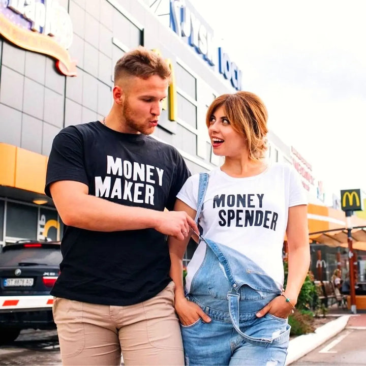 Couple shirts with bold contrast—black tee reads 'Money Maker' in white, white tee says 'Money Spender' in black. A fun power-pair look for couples who balance the books their way. From CouplesChoices.com.