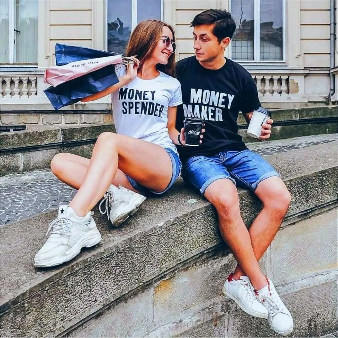 Couple shirts with bold contrast—black tee reads 'Money Maker' in white, white tee says 'Money Spender' in black. A fun power-pair look for couples who balance the books their way. From CouplesChoices.com.