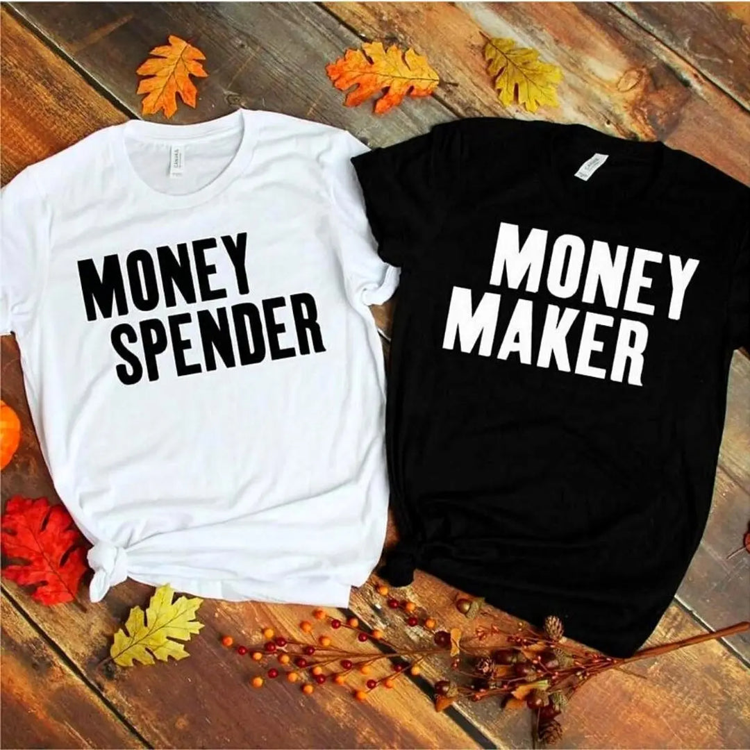 Couple shirts with bold contrast—black tee reads 'Money Maker' in white, white tee says 'Money Spender' in black. A fun power-pair look for couples who balance the books their way. From CouplesChoices.com.