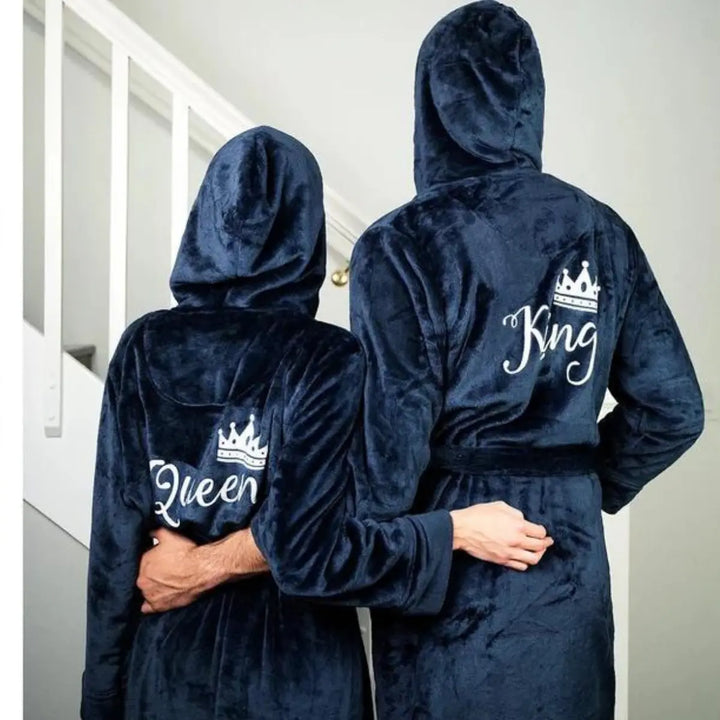 Couple wearing matching plush navy blue hooded bathrobes embroidered with elegant white “King” and “Queen” lettering and crown motifs—luxurious, cozy loungewear designed by CouplesChoices.com for modern royalty.