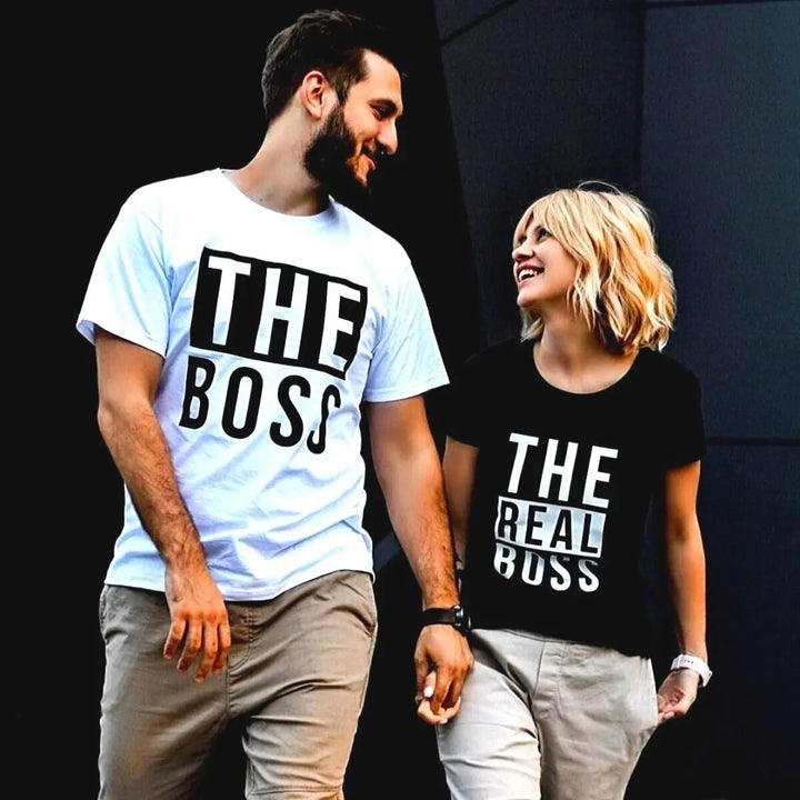 Couples matching graphic tees from CouplesChoices.com—his reads “THE BOSS” in bold black on white, hers says “THE REAL BOSS” in bold white on black. A playful and confident way to show off relationship dynamics with style.
