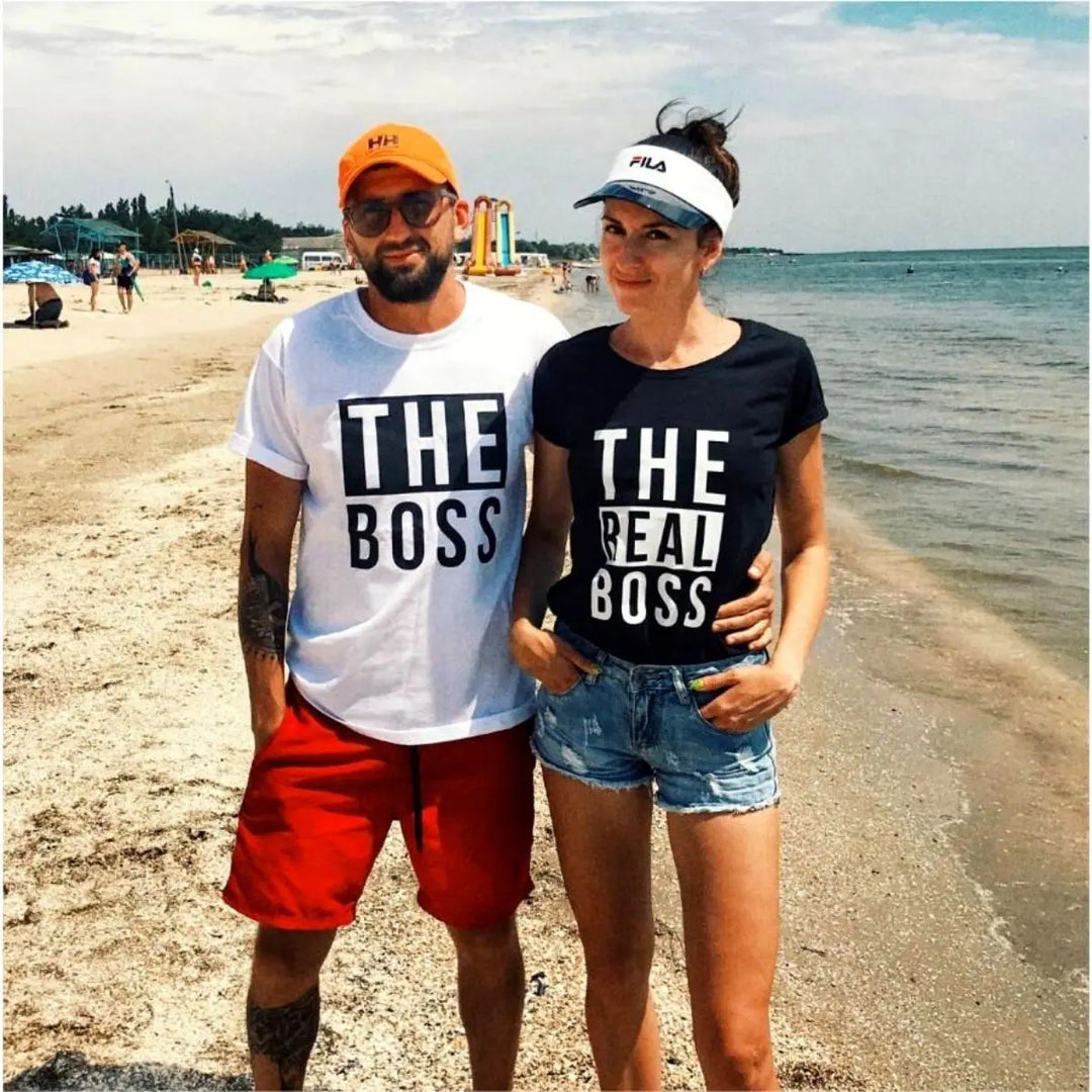 Couples matching graphic tees from CouplesChoices.com—his reads “THE BOSS” in bold black on white, hers says “THE REAL BOSS” in bold white on black. A playful and confident way to show off relationship dynamics with style.