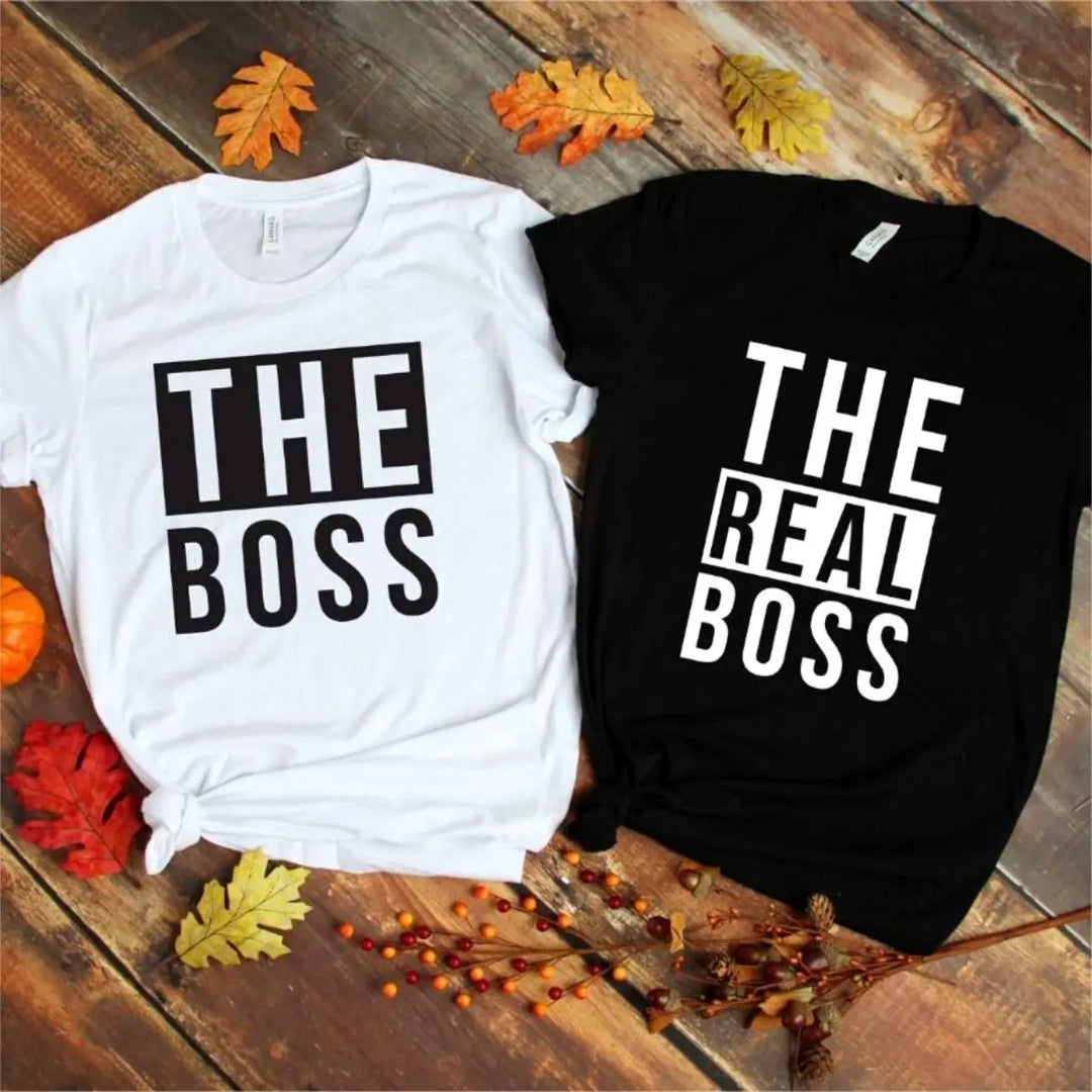 Couples matching graphic tees from CouplesChoices.com—his reads “THE BOSS” in bold black on white, hers says “THE REAL BOSS” in bold white on black. A playful and confident way to show off relationship dynamics with style.
