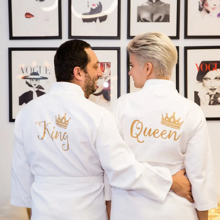 Couples wearing matching white waffle-knit cotton robes featuring gold embroidered “King” and “Queen” with crown motifs, showcasing elegant, coordinated loungewear designed for comfort, romance, and luxury by CouplesChoices.com.