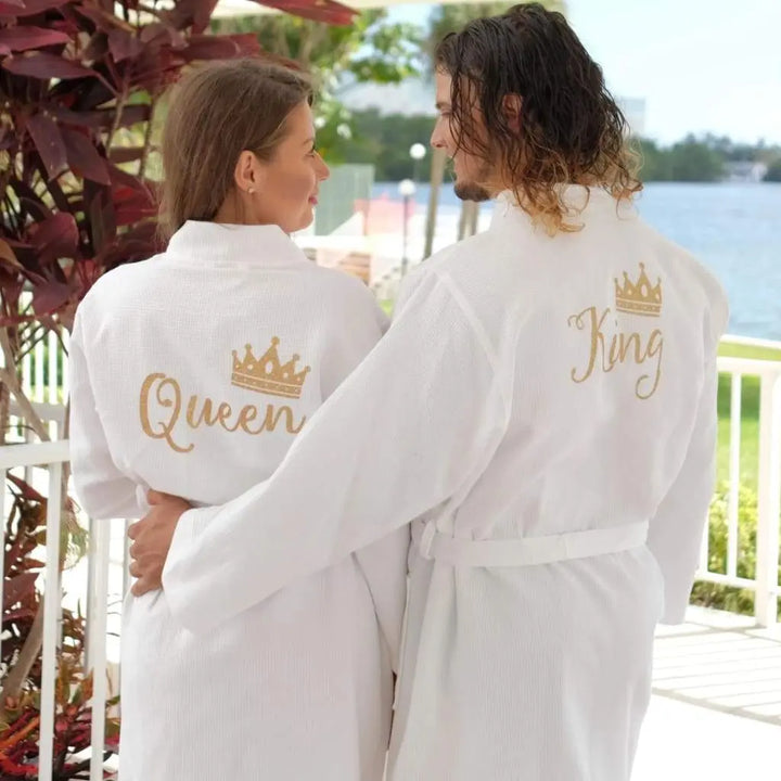 Couples wearing matching white waffle-knit cotton robes featuring gold embroidered “King” and “Queen” with crown motifs, showcasing elegant, coordinated loungewear designed for comfort, romance, and luxury by CouplesChoices.com.