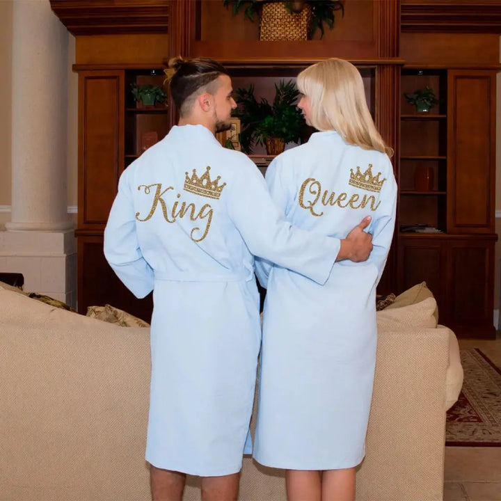 Couples wearing matching white waffle-knit cotton robes featuring gold embroidered “King” and “Queen” with crown motifs, showcasing elegant, coordinated loungewear designed for comfort, romance, and luxury by CouplesChoices.com.