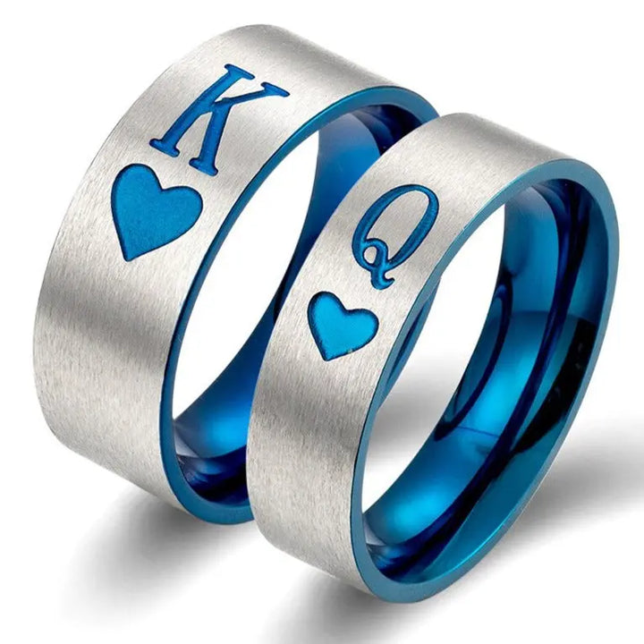 Elegant Royal Harbour Rings from CouplesChoices.com, featuring brushed silver bands with bold blue heart inlays and 'K' & 'Q' engravings—symbolizing King and Queen. A striking emblem of love, loyalty, and regal partnership.