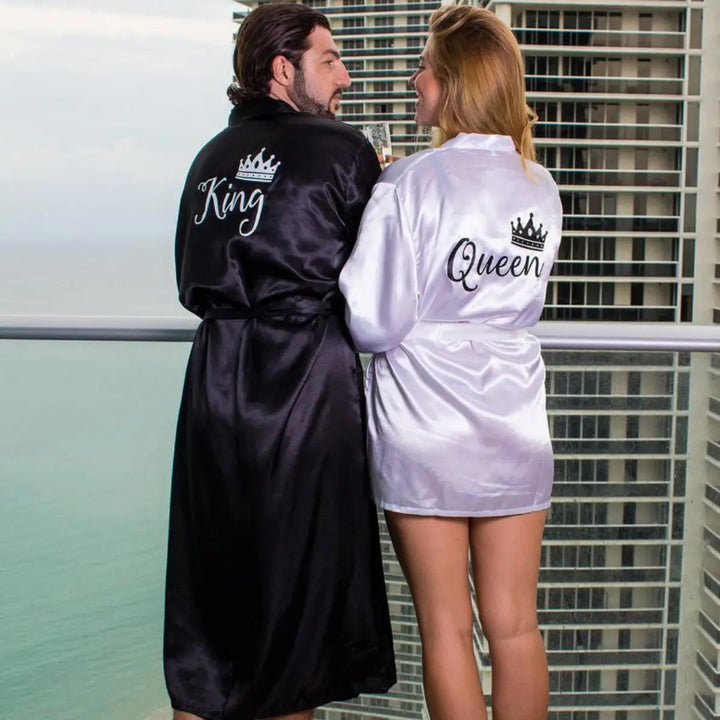 Luxurious satin couple’s robes from CouplesChoices.com, featuring silky black “King” and pearlescent white “Queen” designs embroidered with elegant crown accents—romantic, lightweight loungewear for modern royalty and elevated intimacy.