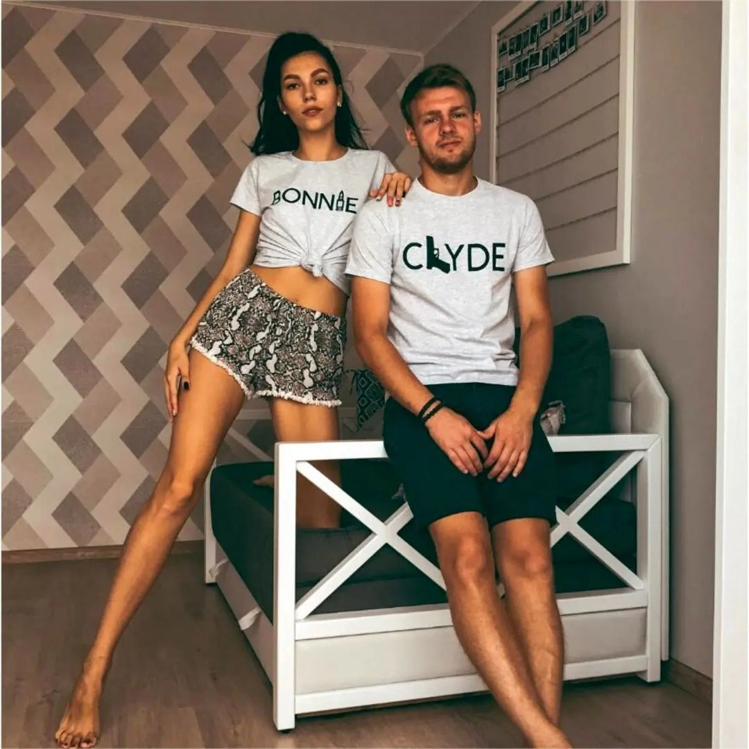 Matching Bonnie & Clyde couple shirts in soft heather grey, featuring bold black text with a gun and bullet design. Perfect for ride-or-die couples who love bold style and iconic vibes. Exclusively from CouplesChoices.com.