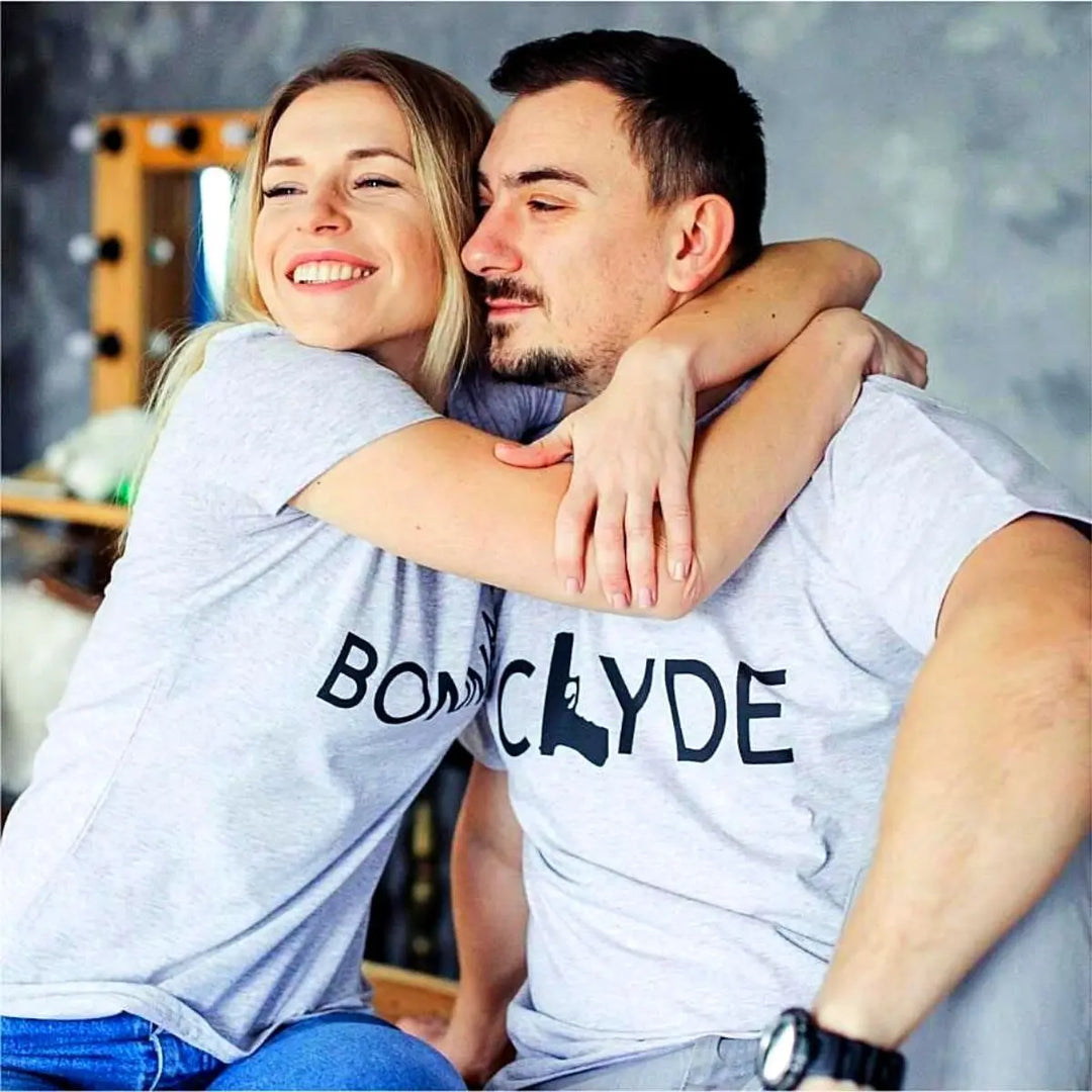 Matching Bonnie & Clyde couple shirts in soft heather grey, featuring bold black text with a gun and bullet design. Perfect for ride-or-die couples who love bold style and iconic vibes. Exclusively from CouplesChoices.com.