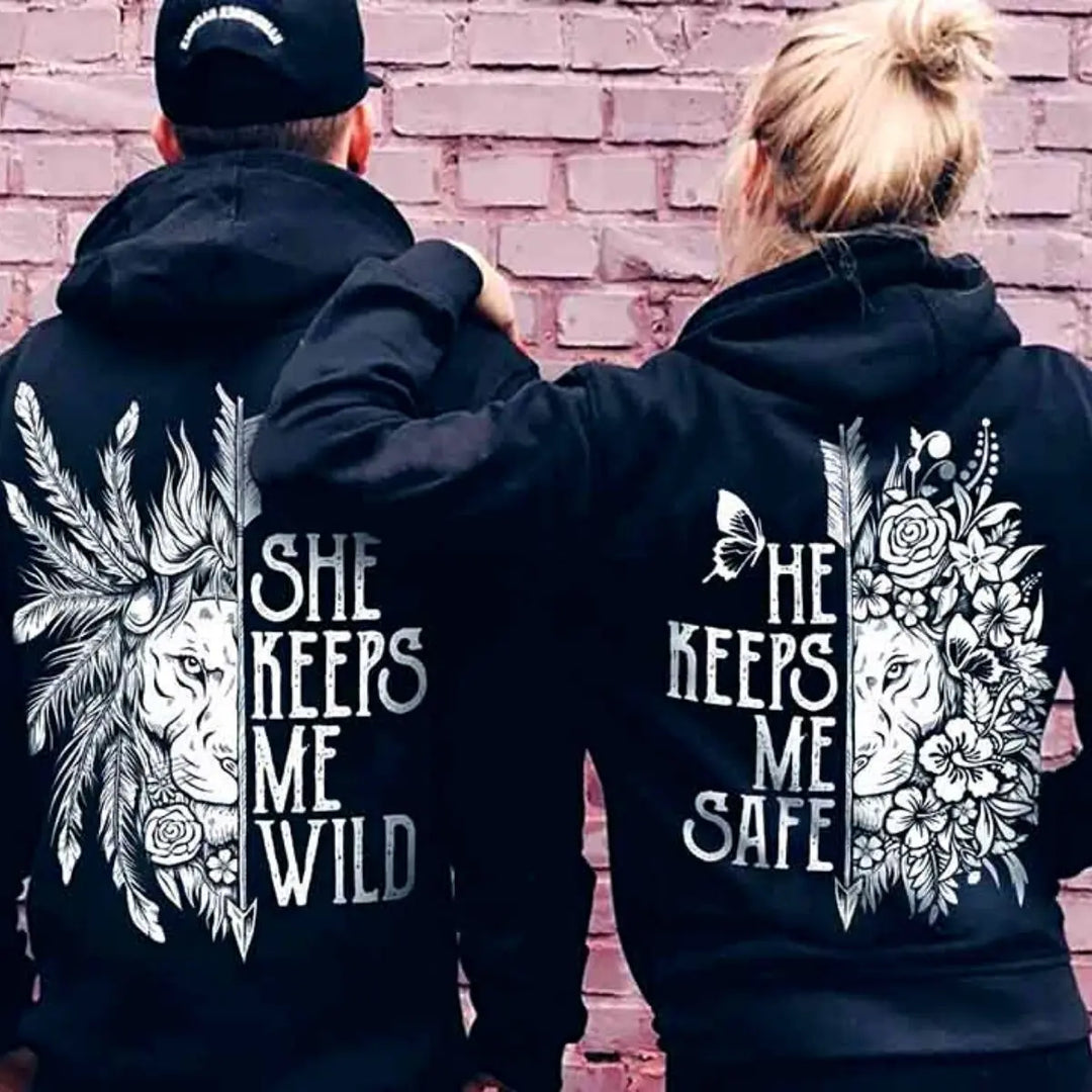 Matching black couple hoodies from CouplesChoices.com featuring powerful lion-themed designs — “She Keeps Me Wild” with feathers and “He Keeps Me Safe” with floral elements. A bold, symbolic set for couples who balance passion with protection.