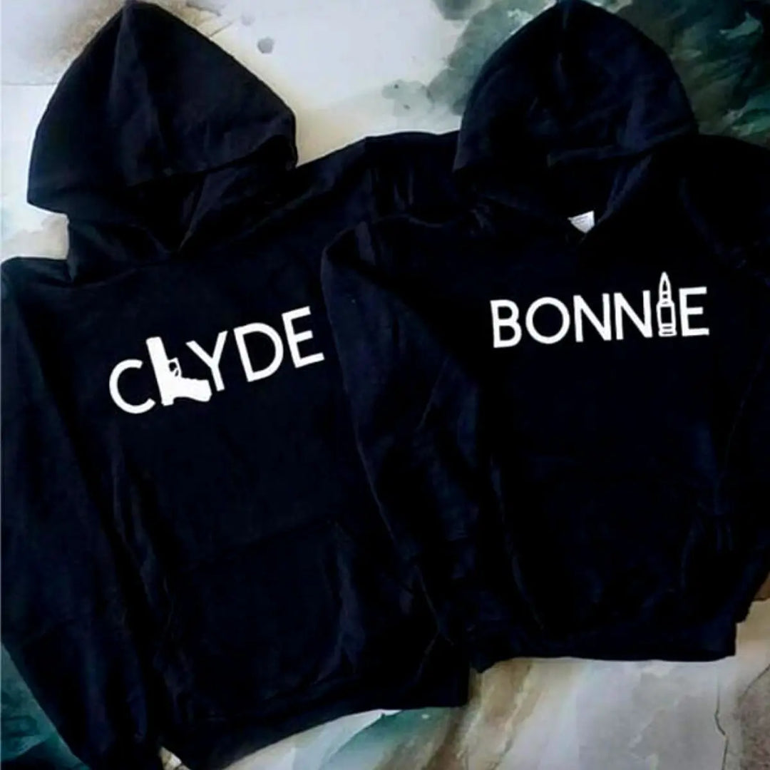 Matching black couple hoodies from CouplesChoices.com with bold white text — “BONNIE” featuring a bullet graphic and “CLYDE” with a gun silhouette. A daring and stylish set for couples who embrace loyalty, edge, and legendary love.