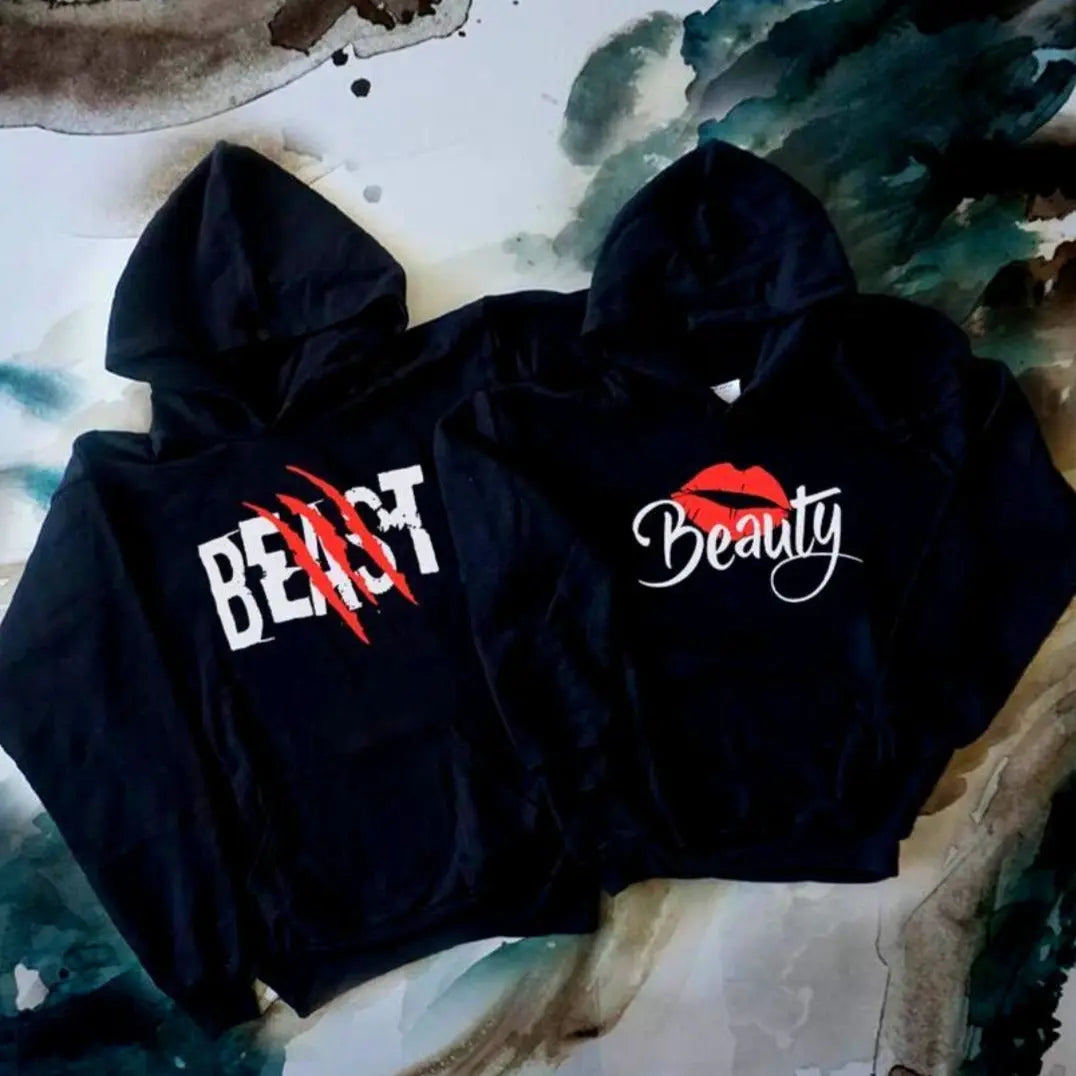 Matching black couple hoodies from CouplesChoices.com with bold white text—his reads “BEAST” with red claw marks, and hers says “Beauty” with a red lipstick kiss graphic. A fun, edgy set for couples who embrace fierce love and playful contrasts.