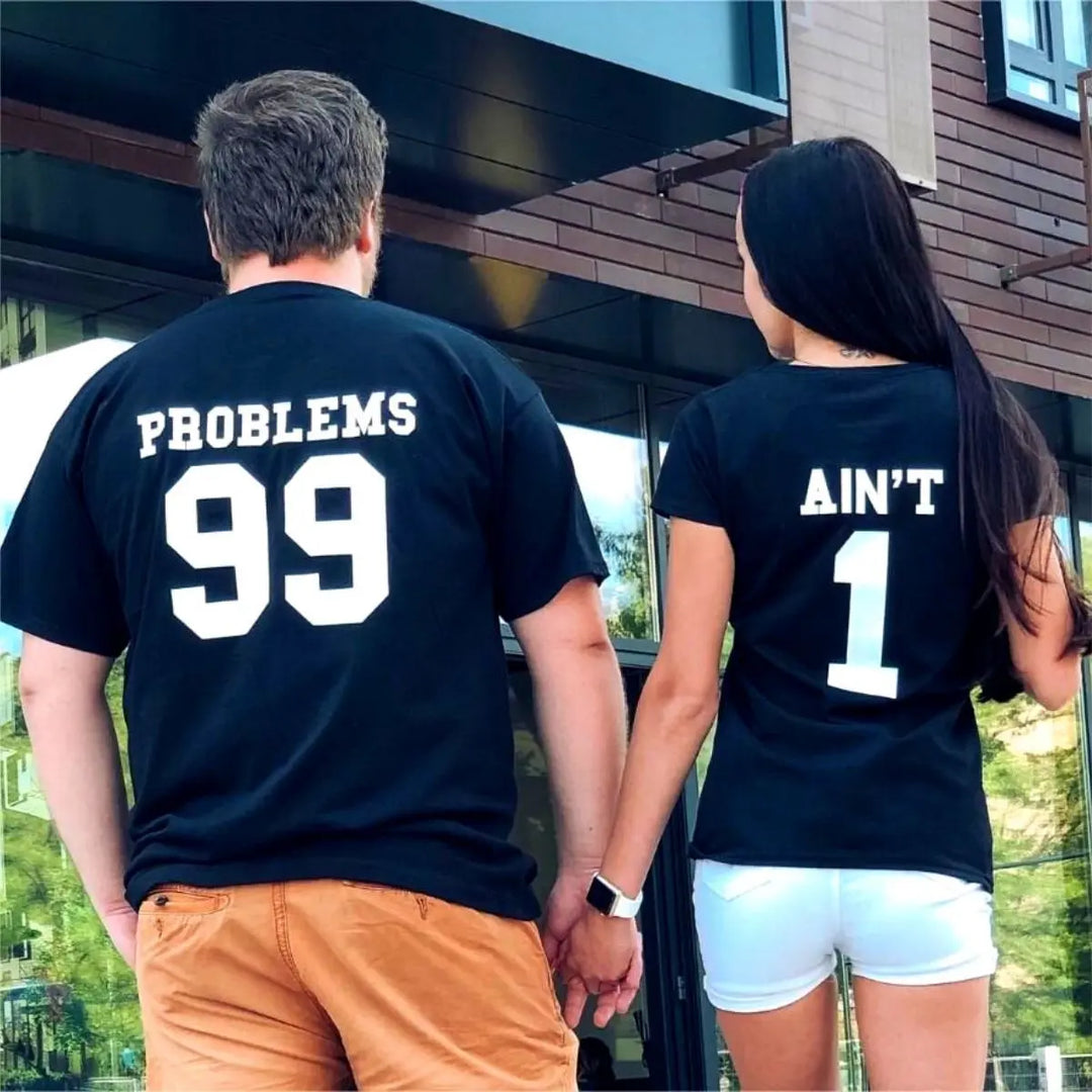 Matching black couple shirts—his reads '99 Problems' and hers answers 'Ain’t 1' in varsity-style white print. A playful nod to love and loyalty, exclusively from CouplesChoices.com.