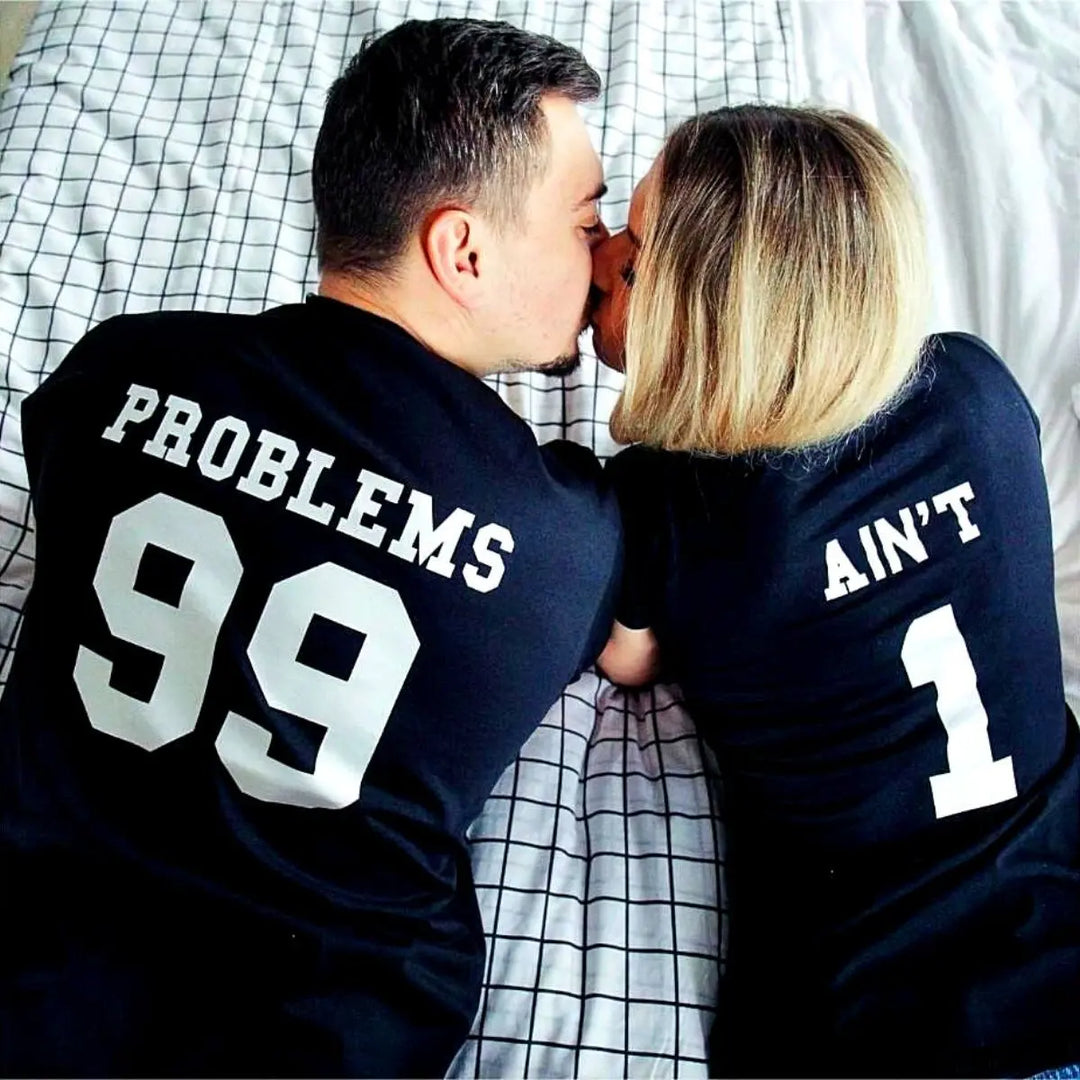 Matching black couple shirts—his reads '99 Problems' and hers answers 'Ain’t 1' in varsity-style white print. A playful nod to love and loyalty, exclusively from CouplesChoices.com.